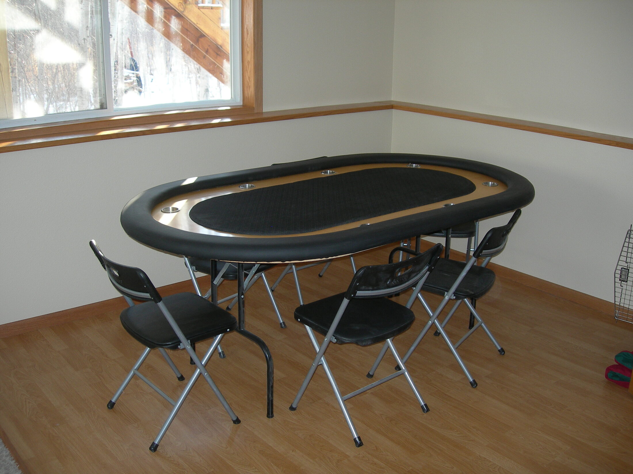 Finished DIY racetrack poker table with padded black rails, hardwood raceway, cup holders, and folding chairs in a home game room