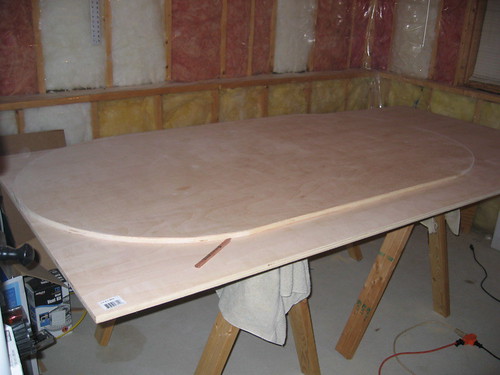 Oval plywood cutout for a poker table base resting on sawhorses in a garage workshop